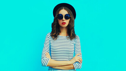 Portrait of stylish young woman model posing wearing a striped t-shirt and summer straw round hat on blue background