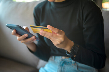 A happy young woman is shopping online via smart phone , holding credit card..
