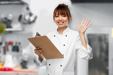 cooking, culinary and people concept - happy smiling female chef with clipboard waving hand over...