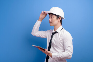 Portrait of confident male engineer wearing a white helmet  using tablet over blue  background studio