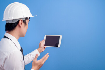 Portrait of confident male engineer wearing a white helmet  using tablet over blue  background studio