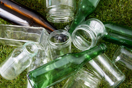 recycling, garbage disposal, environment and ecology concept - close up of empty used glass bottles and jars on grass