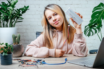 A teenager girl holding a sensor chip studying robotics at home, stem and arduino coding classes...