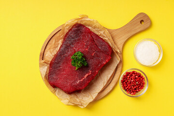 Concept of cooking with raw beef steak on yellow background