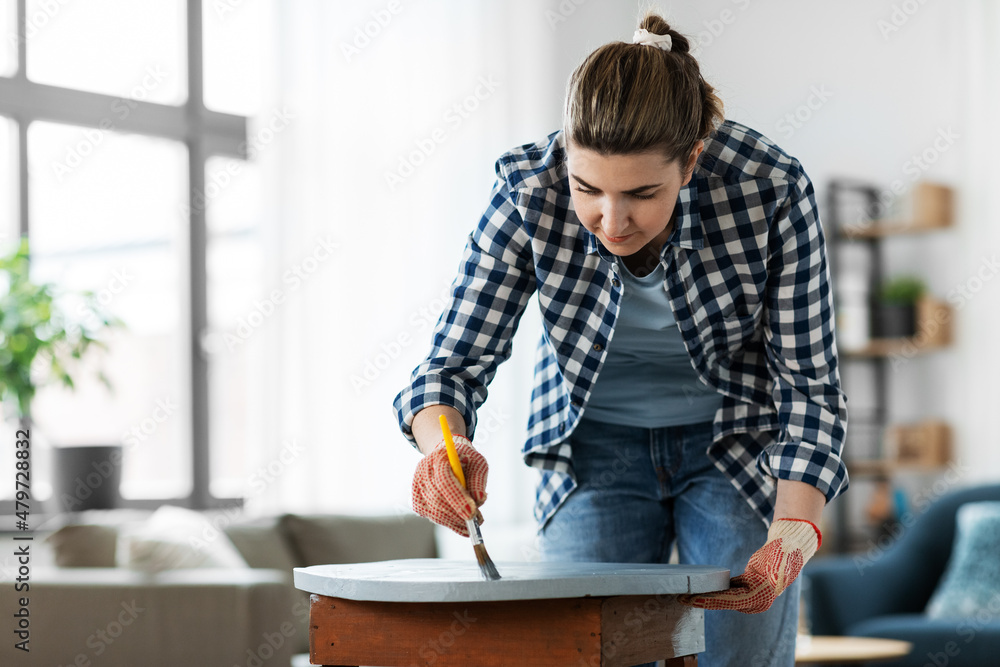 Wall mural renovation, diy and home improvement concept - woman in gloves with paint brush painting old wooden table to grey color