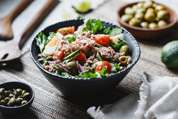 Canned tuna salad with fresh vegetables, capers and olives in a black bowl. Healthy lunch or dinner.