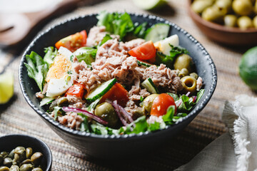 Fototapeta Canned tuna salad with fresh vegetables, capers and olives in a black bowl. Healthy lunch or dinner. obraz