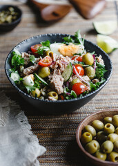 Canned tuna salad with fresh vegetables, capers and olives in a black bowl. Healthy lunch or dinner.