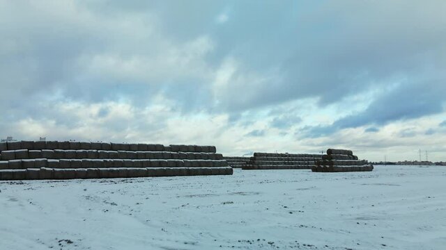Flying over a snowy field. Straw bales are stacked. Traces of agricultural tillage are visible under the snow. Aerial photography.