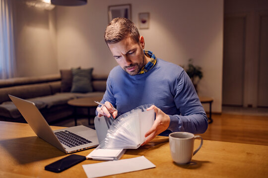 Finances, bills, family budget, and economy. A young man sitting at home with a poly envelope in his hands and looking at bills. He is going to pay bills online on the laptop.