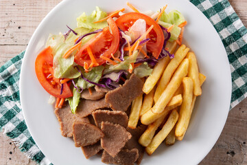 Plate of kebab, vegetables and french fries on wooden table	