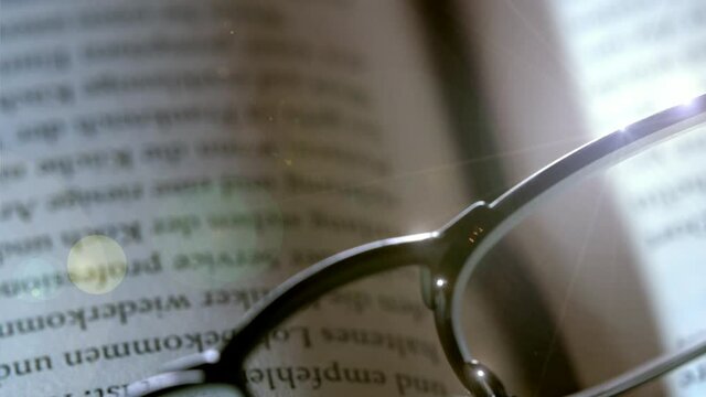 Close-up of reading glasses on an open book, with artificially inserted lens reflections