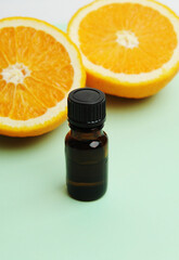 Essential oil in dark glass bottle on light green background. Fresh orange cut in half. Cosmetic, healthy concept