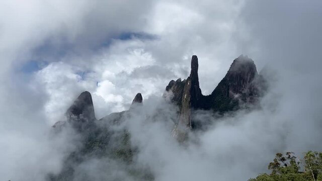 Thick rising clouds obscuring Brazilian panoramic landscape of mountain range Serra dos Orgaos in Teresopolis, Rio de Janeiro with Dedo de Deus, Gods finger, peak in the middle and clouds behind