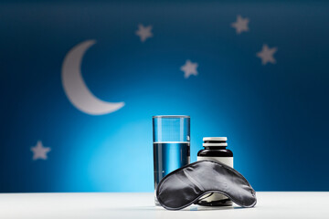 sleep disorder, bedtime and object concept - close up of eye mask, glass of water and soporific...