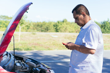 Older man texting by the broken down car.