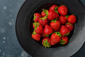 Strawberry ripe. Fresh red strawberry in black plate or bowl on dark stone background with copy space. Top view. Mock up.