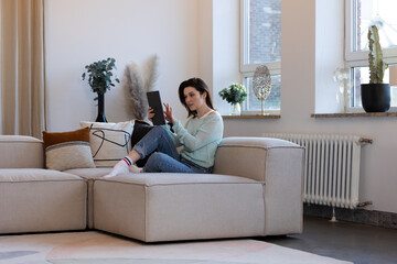 Woman with tablet computer on sofa browsing the internet in her living room, student relaxing at home with technology