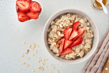 Oatmeal porridge with strawberry slices, nuts almonds and honey in bowl for Valentines Day on grey table. Concept for romantic breakfast or meal. Top view. Mock up.