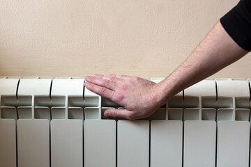 man's hand on a white battery at home, warmed by the battery, trying or warm