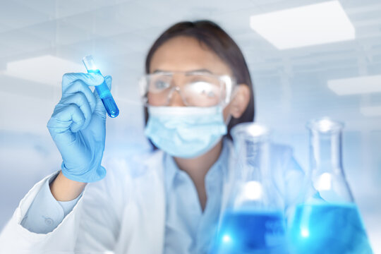 Blurred woman chemist holding a test-tube examines chemical solution in laboratory. Biochemistry science research and development concept.
