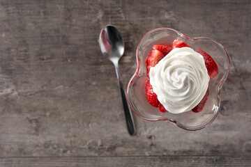 Strawberries and whipped cream in ice cream glass on wooden table. Copy space