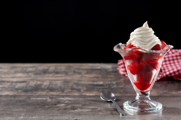 Strawberries and whipped cream in ice cream glass on wooden table. Copy space