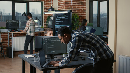 Senior developer coding on laptop at desk with computer screens parsing code in software agency....