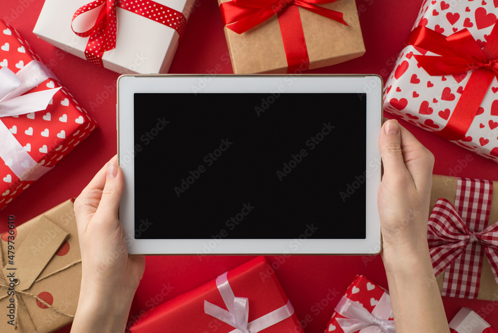 Wall mural First person top view photo of valentine's day decorations woman's hands holding tablet computer over gift boxes on isolated red background with empty space