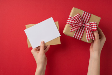 Obraz premium First person top view photo of valentine's day decor girl's hands holding letter envelope and craft paper giftbox with checkered ribbon bow on isolated red background with blank space