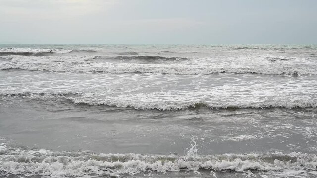 Muddy sea water after the rain. Stormy weather on the coast. Waves of the sea with sandy brown and grey color. 