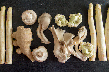 Raw  ingredients set for cooking on black background: white asparagus, mushrooms, ginger, cauliflower. Overhead.