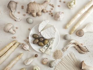 Plant based modern still life flat lay. Raw vegan ingredients set for cooking on white background: asparagus, mushrooms, eggs, noodles and brie cheese.