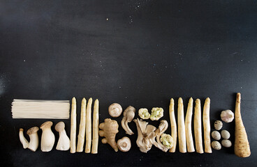 Plant based modern still life flat lay. Raw  ingredients set for cooking on black background: white asparagus, mushrooms, eggs, noodles and ginger on black background. Overhead.