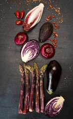 Plant based modern flat lay set collection red purple vegetables on black background. Asparagus, red cabbage, avocado, eggplants, onion. Healthy food concept. Overhead. Top view.