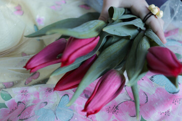 A bouquet of pink tulips lies on the girl's lap, she holds them with a small hand, on which she is wearing a ring. International Women's Day, 8 March, Spring Holiday.