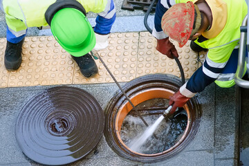 workers  with helmets and safety clothing  for cleaning with water pressure the sewerage and canalization pipes  in city street - obrazy, fototapety, plakaty