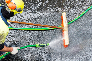 construction worker with broom and water pressure to cleaning road in city at contruction site