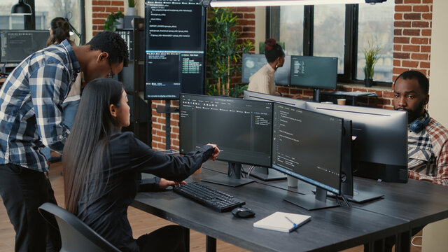 Mixed team of programmers analyzing source code pointing at screens comparing algorithm with user interface on digital tablet. Software developers working on cyber security group project.