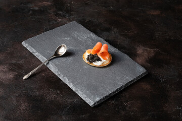 Blini pancake with black sturgeon caviar and a slice of salmon on a slate