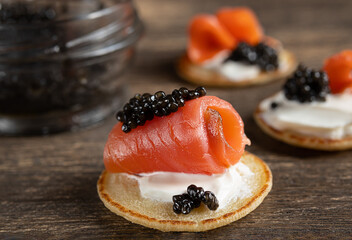 Salmon and black sturgeon caviar on blini pancakes on a wooden table close-up