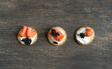 Three blini pancakes with black sturgeon caviar and salmon on a wooden table