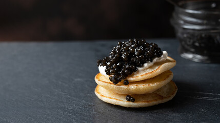 Black caviar on a stack of pancakes on a dark gray background with copy space