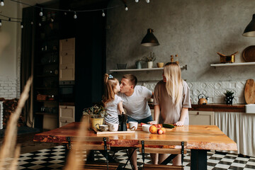 A happy family with one child having breakfast laughing sitting at the dining table in a loft-style kitchen in a cozy house. Pregnant mom dad and little daughter cook together. Selective focus