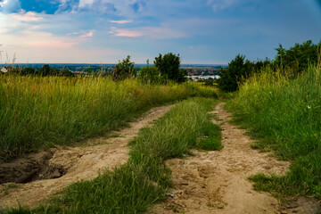 Obraz premium A bad dirt road, a road overgrown with grass on the background of beautiful clouds 