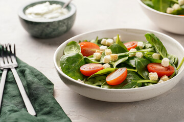 Salad bowl with fresh green spinach, cherry tomatoes, croutons and sour cream dressing on a grey stone surface