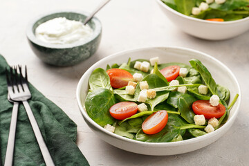 Salad bowl with fresh green spinach, cherry tomatoes, croutons and sour cream dressing on a grey stone surface
