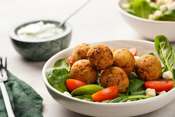 Salad bowl with chickpea falafel, fresh green spinach, cherry tomatoes, croutons and sour cream dressing on a grey stone surface
