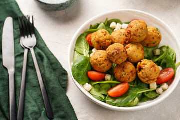 Salad bowl with chickpea falafel, fresh green spinach, cherry tomatoes, croutons and mint yoghurt dressing on a grey stone surface