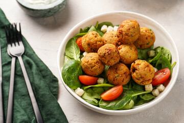 Salad bowl with chickpea falafel, fresh green spinach, cherry tomatoes, croutons and mint yoghurt dressing on a grey stone surface
